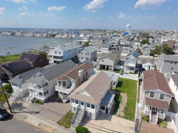Aerial view of a coastal neighborhood of beach cottages with three-story porches, stairs to sidewalks, and water in the background.