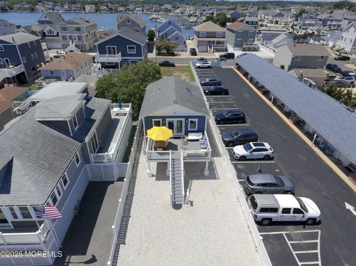 Aerial view of a seaside neighborhood with a blue house on a deck featuring a yellow umbrella and patio furniture.