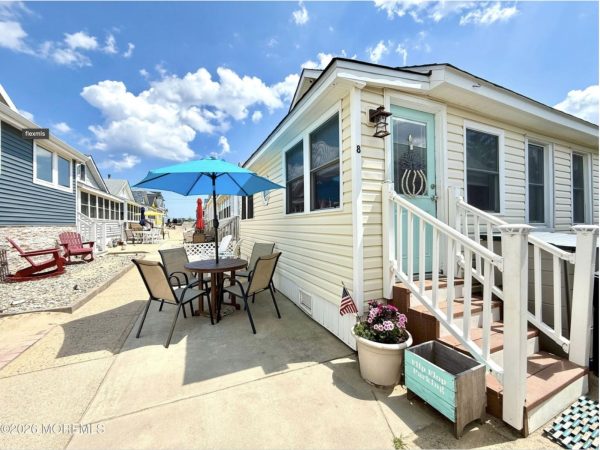Outdoor seating area between beach cottages with a blue patio umbrella, round table and chairs on a sunny walkway.