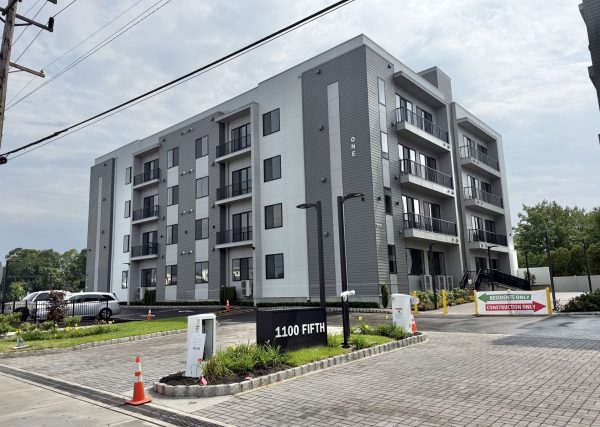 Modern six-story apartment building with gray and white panels and balconies; construction barriers and a '1100 Fifth' sign in foreground.