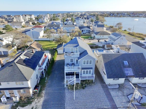 Aerial view of a seaside neighborhood with pastel houses, backyards, and a blue ocean in the distance.