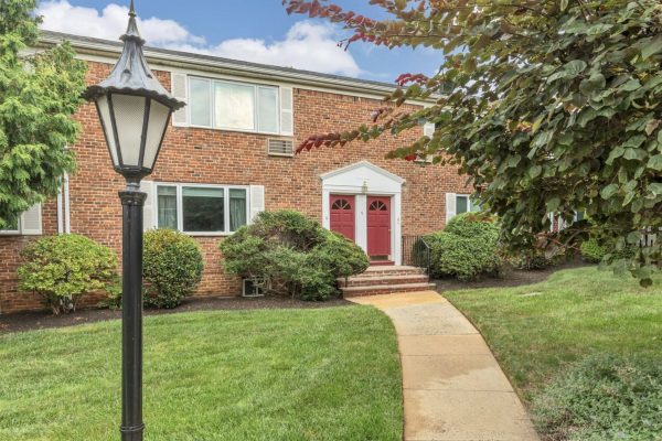 Red double doors of a brick apartment building with white trim, framed by shrubs and a curved walkway.